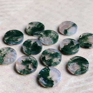 May include: Twelve round, flat, green and white agate cabochons. The cabochons have a translucent, milky white base with green moss-like inclusions.