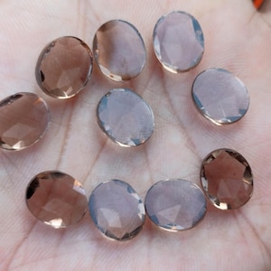 May include: Ten oval-shaped, faceted, smoky quartz gemstones. The stones are translucent and have a light brown color.