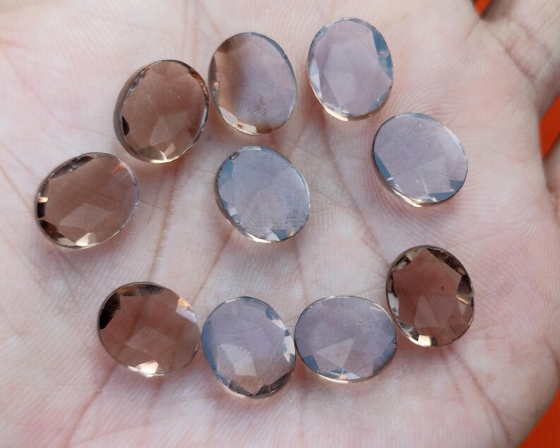 May include: Ten oval-shaped, faceted, smoky quartz gemstones. The stones are translucent and have a light brown color.