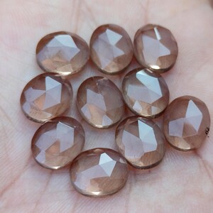 May include: Ten faceted oval-shaped gemstones in shades of brown and pink. The gemstones are smooth and polished.