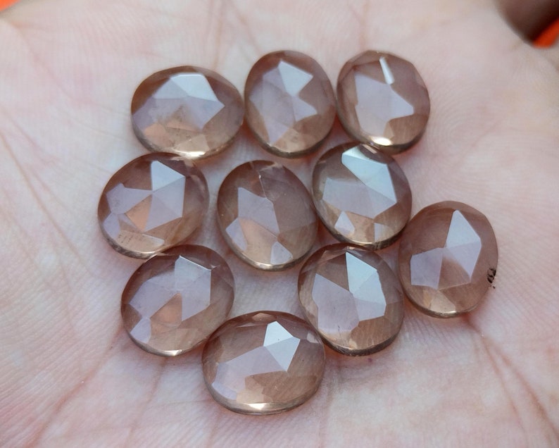 May include: Ten faceted oval-shaped gemstones in shades of brown and pink. The gemstones are smooth and polished.
