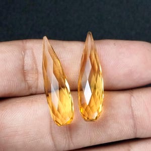 May include: Two teardrop-shaped, faceted, topaz gemstones in a golden yellow color.