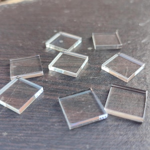 Könnte beinhalten: Neun transparente Glassquadrate in verschiedenen Größen auf einer dunkelbraunen Holzoberfläche.