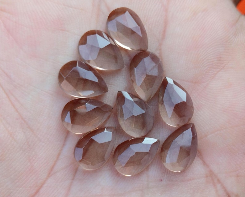 Pu&ograve; includere: Una collezione di dieci perle di pietra preziosa sfaccettate a forma di goccia di colore marrone chiaro. Le perle sono traslucide e hanno un leggero luccichio.