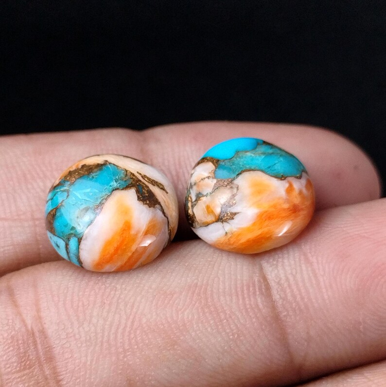 May include: Two round, cabochon-cut turquoise stones with orange and brown matrix. The stones have a smooth, polished surface.