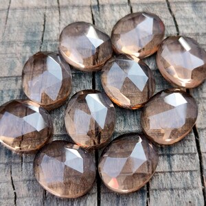 May include: Ten faceted smoky quartz stones in various sizes and shapes, arranged in a circular pattern on a wooden surface.