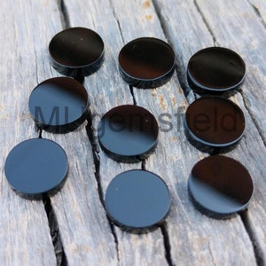 Peut inclure: Neuf pierres précieuses rondes en cabochon noires sur une surface en bois.