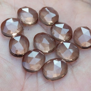 May include: Ten faceted, translucent, light brown gemstones with a shimmery finish. The gemstones are oval shaped and have a smooth, polished surface.
