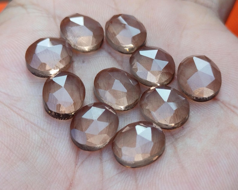 May include: Ten faceted, translucent, light brown gemstones with a shimmery finish. The gemstones are oval shaped and have a smooth, polished surface.