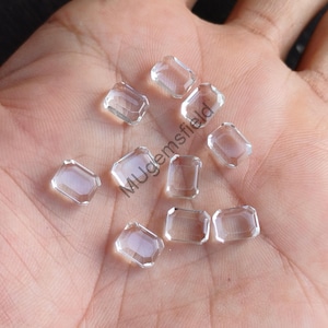 Puede incluir: Una colección de gemas claras y facetadas con talla esmeralda. Las gemas transparentes reflejan la luz, mostrando sus formas geométricas. Las gemas están dispuestas sobre un fondo neutro, resaltando su claridad.