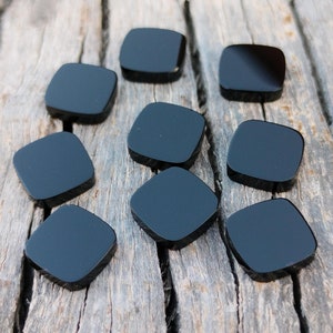 Puede incluir: Diez cabujones de piedra preciosa de forma cuadrada negra, probablemente ónix, dispuestos sobre una superficie de madera.