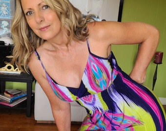 May include: A woman wearing a colorful, abstract print maxi dress with a plunging neckline. The dress has a mix of pink, purple, blue, green, and white colors.