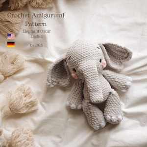 Może przedstawiać: Szydełkowa szara zabawka amigurumi w kształcie słonia z dużymi uszami, trąbą i małymi różowymi policzkami. Widoczny jest tekst "Crochet Amigurumi Pattern" i "Elephant Oscar". Zabawka leży na białej powierzchni.