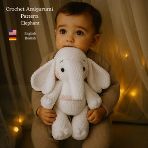 Może przedstawiać: Biały szydełkowy amigurumi słonia z dużymi uszami i trąbą, trzymany przez dziecko. Słoń ma różowe haftowane imię na piersi. Obraz zawiera tekst "Crochet Amigurumi Pattern Elephant".