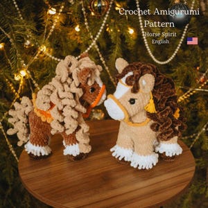 Könnte beinhalten: Zwei gehäkelte Amigurumi-Pferdefiguren in Braun-, Beige- und Weißtönen mit orangefarbenen und gelben Akzenten. Der Text "Crochet Amigurumi Pattern Horse Spirit English" ist sichtbar. Die Pferde werden auf einer Holzoberfläche präsentiert.