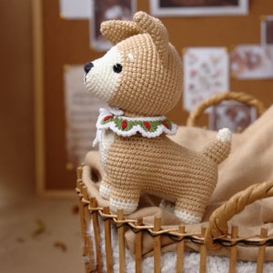 Peut inclure: Un jouet en crochet pour chien de couleur beige et blanc avec un collier vert et rouge. Le jouet est dans un panier en osier.