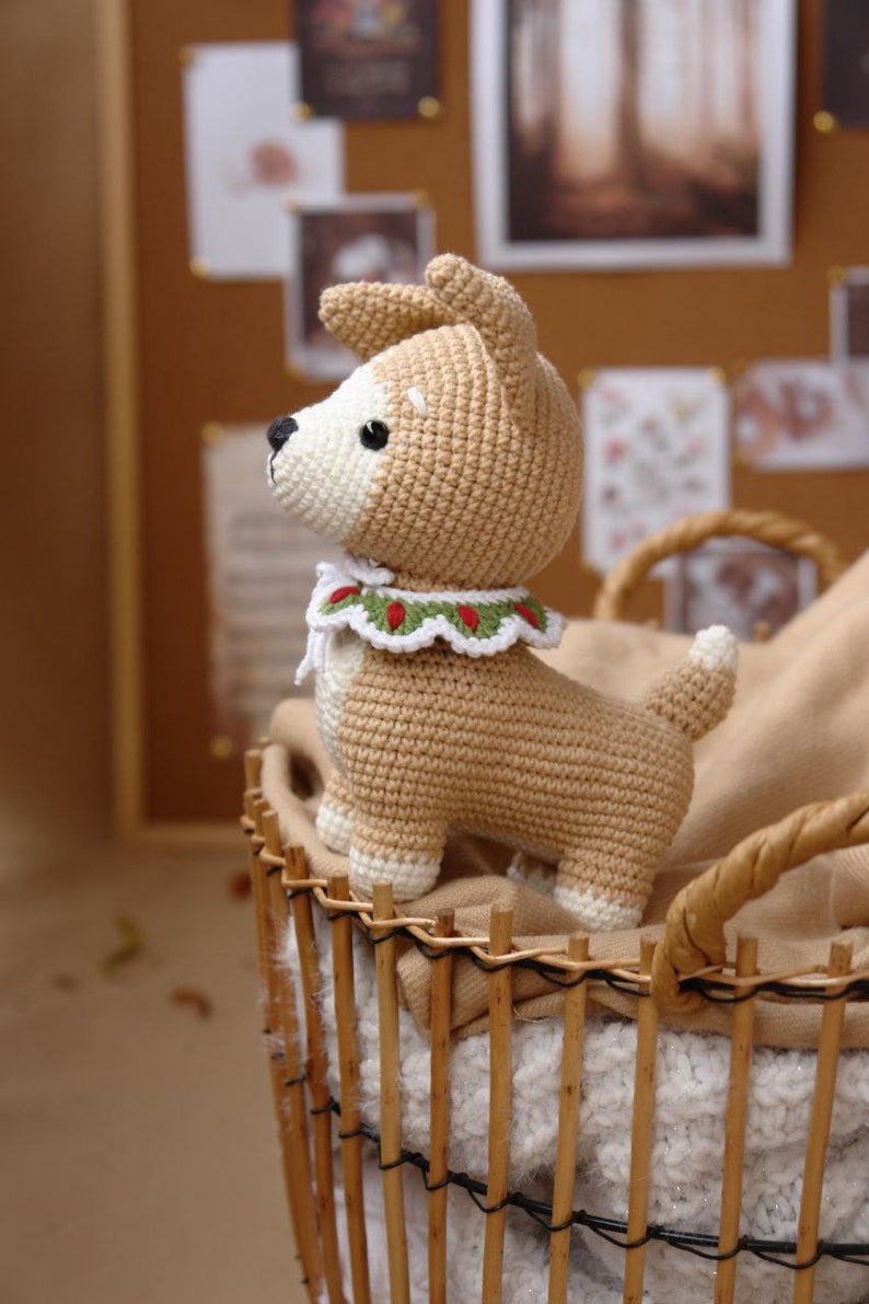 Peut inclure: Un jouet en crochet pour chien de couleur beige et blanc avec un collier vert et rouge. Le jouet est dans un panier en osier.