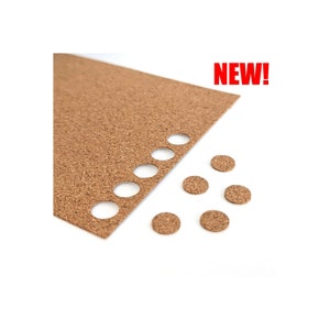 May include: A sheet of brown cork with several round holes cut out.  There are six brown cork circles on a white surface next to the sheet of cork.  The text "NEW!" is in red letters above the cork sheet.