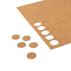 May include: A sheet of corkboard with a row of cut-out circles along the edge. There are several small cork circles scattered below the board.