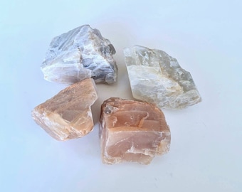 May include: Four pieces of sunstone, two are a light grey color and two are a light brown color. The stones are rough and have a natural, unpolished look.