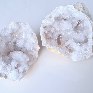 May include: Two white crystal geode halves with a rough exterior and a sparkling white crystal interior.