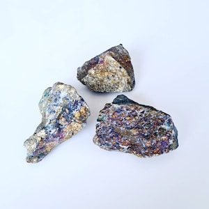 May include: Three rough, irregularly shaped pieces of pyrite, a metallic mineral with a gold-like colour and iridescent hues. The pyrite is displayed on a white background.