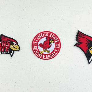 Op de afbeelding: Drie geborduurde patches met het merk Illinois State University. De linker patch toont de tekst Redbirds en een kardinaalkop. Het midden is een rond embleem met een kardinaal en de tekst Illinois State University 1857. Rechts is een kardinaalkop te zien.