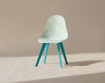 May include: A miniature paper chair with a light blue seat and teal blue legs.