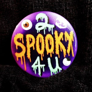 May include: A purple button with a dripping orange and green design that says "2 Spooky 4 U" with eye and skull graphics.