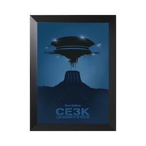 Puede incluir: Un póster enmarcado con fondo azul que presenta una silueta negra de una nave espacial flotando sobre una montaña. El texto "Steven Spielberg's CLOSE ENCOUNTERS OF THE THIRD KIND" está impreso en blanco en la parte inferior del póster.