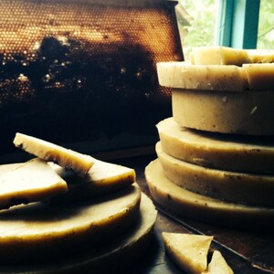 May include: A stack of round, light brown beeswax discs, with a few smaller pieces of beeswax on a plate to the left. The beeswax is a natural product from honeybees.