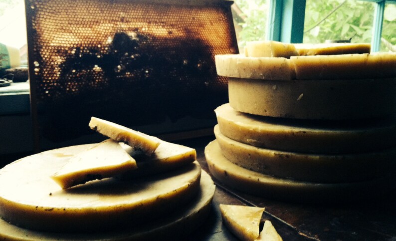 May include: A stack of round, light brown beeswax discs, with a few smaller pieces of beeswax on a plate to the left. The beeswax is a natural product from honeybees.
