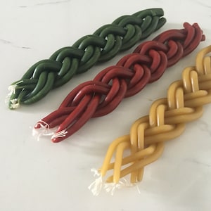Puede incluir: Tres velas trenzadas en verde, rojo y amarillo. Las velas están trenzadas juntas en un estilo tradicional.