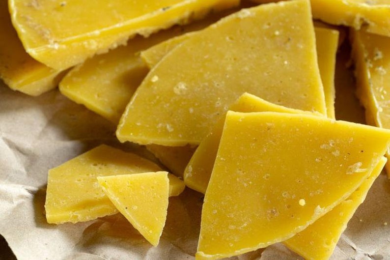 May include: Close-up of several pieces of yellow beeswax, broken into irregular shapes, on a brown paper surface.