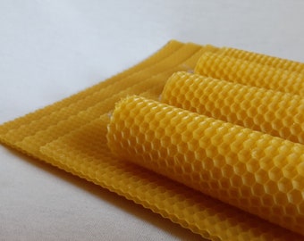May include: A close-up of several yellow beeswax sheets and honeycomb candles. The sheets are stacked on top of each other, and the candles are rolled up.