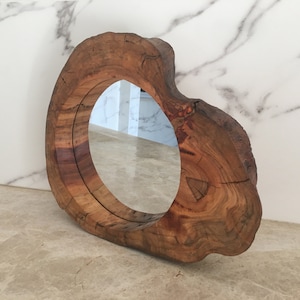 May include: A circular mirror with a wooden frame. The frame is crafted from a section of a tree trunk, displaying the wood's grain and knots. This mirror is a decorative element for the home.