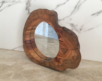May include: A circular mirror with a wooden frame. The frame is crafted from a section of a tree trunk, displaying the wood's grain and knots. This mirror is a decorative element for the home.