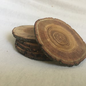 May include: A set of five wooden coasters, each with a unique wood grain pattern and a natural bark edge. The coasters are stacked on top of each other, showcasing the different wood grain patterns.