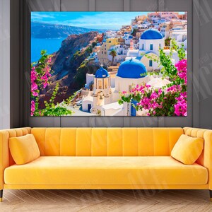 May include: A scenic photograph of a whitewashed village with blue domed churches, nestled on a cliff overlooking a turquoise sea. Lush green foliage and vibrant pink flowers add a touch of color to the scene.