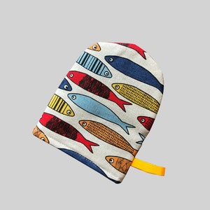 Peut inclure: Un gant de cuisine blanc avec un motif de poissons colorés et une boucle de suspension jaune. Les poissons sont rouges, bleus, jaunes et orange.