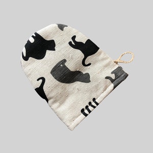 Op de afbeelding: Een witte katoenen ovenwant met een zwart kattenontwerp. De ovenwant heeft een lus om op te hangen.