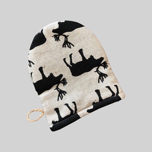 Puede incluir: Un guante de horno blanco con un patrón de renos blanco y negro. El guante tiene un lazo para colgar.