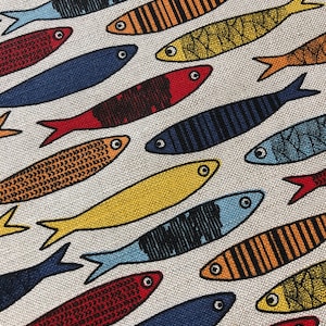 May include: A white fabric with a repeating pattern of colorful fish. The fish are in various shades of blue, red, yellow, and orange. Some of the fish have stripes, while others have a more textured pattern.