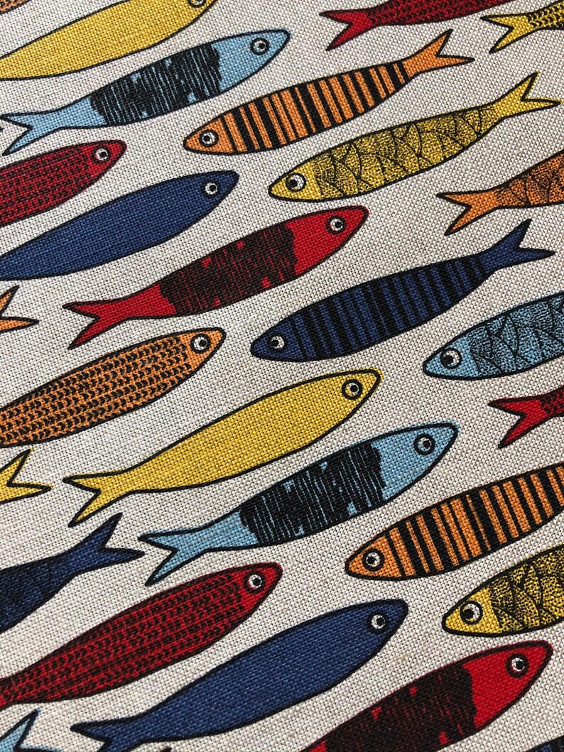 May include: A white fabric with a repeating pattern of colorful fish. The fish are in various shades of blue, red, yellow, and orange. Some of the fish have stripes, while others have a more textured pattern.