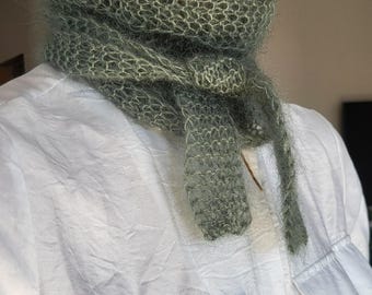 Peut inclure: Une écharpe vert sauge à tissage ouvert est drapée autour du cou. L'écharpe a une texture douce et floue et de longues extrémités pendantes. L'écharpe est portée sur une chemise blanche boutonnée avec deux poches avant.