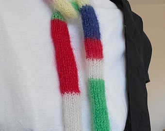 May include: A colourful knitted scarf with stripes of red, white, blue, green, orange and purple. The scarf is tied around the neck of a person wearing a white shirt.