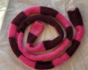 May include: A knitted scarf in a spiral, with alternating bands of bright pink and dark burgundy. The yarn has a soft, fuzzy texture. The scarf is likely handmade and suitable for cold weather.