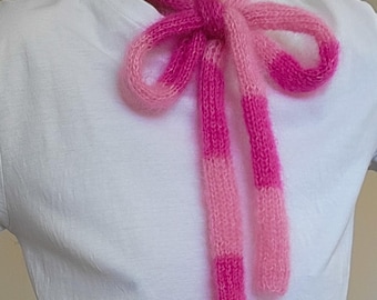 May include: A pink and light pink striped knitted scarf tied in a bow around the neck.