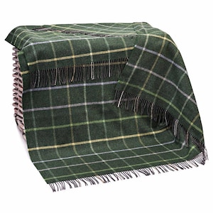 Puede incluir: Una manta a cuadros verdes con borde de flecos está sobre una cesta de mimbre. La manta presenta un patrón de cuadros clásico en tonos verdes, blancos y amarillos. La franja es negra y blanca.