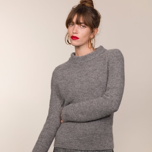 Puede incluir: Un suéter gris de punto con cuello alto y mangas largas. El suéter tiene un patrón de punto texturizado.